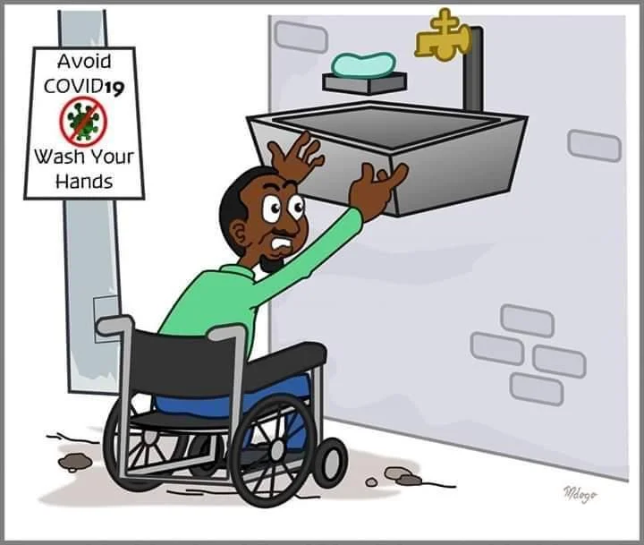 The cartoon depicts a dark-skinned man in a wheelchair who lifts up his arms to wash his hands in the basin, which is still too high for him. The sign on the wall near the basin says “Avoid COVID19. Wash your hands”